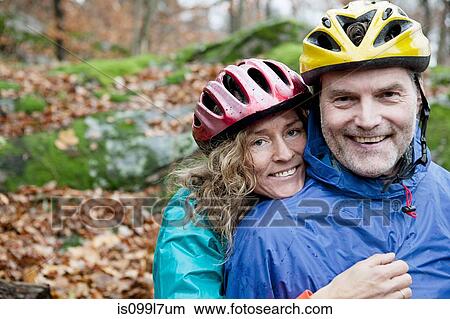 Picture - Portrait of mature couple wearing cycling helmets in forest. Fotosearch