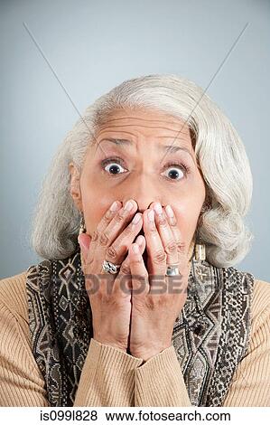 Stock Photo - Portrait of senior woman covering mouth with hands in studio. Fotosearch