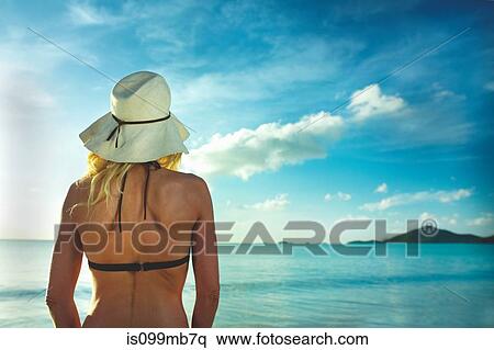Stock Photography - Rear view of woman in sunhat looking out to sea. Fotosearch