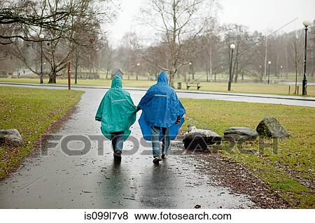 Stock Photo - Senior couple in waterproof clothing walking through park. Fotosearch