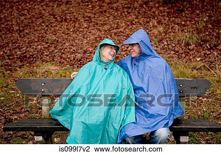 Stock Image - Senior couple sitting on park bench wearing waterproofs. Fotosearch