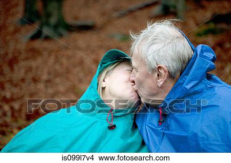 Picture - Senior couple wearing waterproofs and kissing. Fotosearch