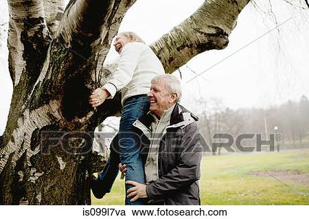 Stock Image - Senior man helping woman climb tree in park. Fotosearch