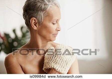 Stock Image - Senior woman exfoliating with mitt. Fotosearch
