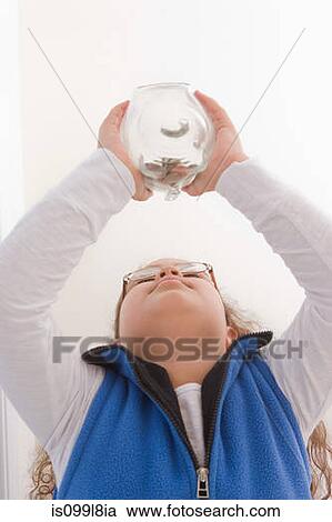 Stock Image - Young girl holding piggy bank, low angle. Fotosearch