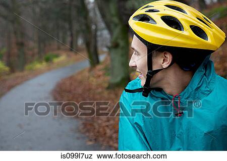Stock Photo - Young man wearing cycling helmet on forest path and looking over shoulder. Fotosearch