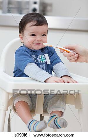 Stock Image - Adult feeding baby boy in high chair. Fotosearch