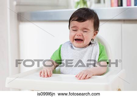 Picture - Baby boy in high chair, crying. Fotosearch