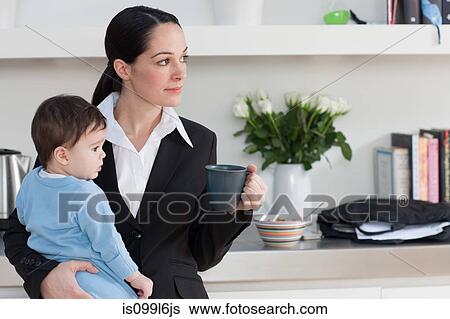 Stock Photograph - Businesswoman holding baby son and coffee cup. Fotosearch