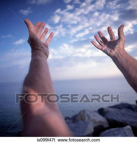 Stock Photograph - Close up of man with arms stretched in yoga pose by the ocean. Fotosearch