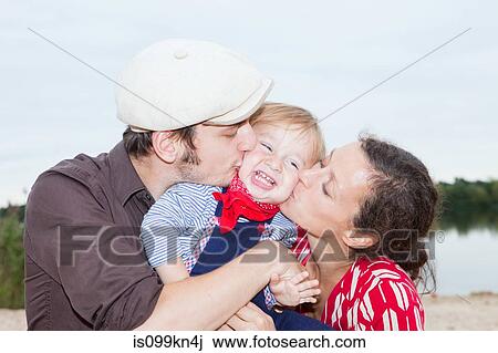 Stock Image - Couple kissing their young son on his cheeks. Fotosearch