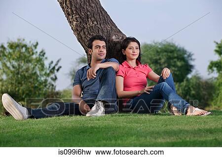 Couple sitting together next to a tree View Large Photo Image Stock Photo - Couple sitting together next to a tree. Fotosearch