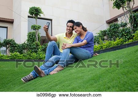 Couple taking a self portrait on a lawn View Large Photo Image Stock Photography - Couple taking a self portrait on a lawn. Fotosearch