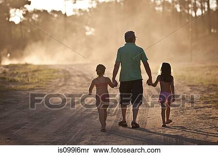 Stock Photography - Father and daughters walking hand in hand on dust road. Fotosearch