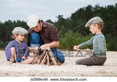 Stock Image - Father and sons making a bonfire on beach. Fotosearch
