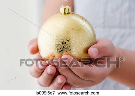 Stock Photo - Girl holding a gold christmas bauble. Fotosearch