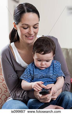 Stock Photo - Mother and baby boy holding remote control. Fotosearch