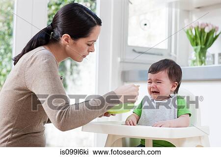 Stock Image - Mother feeding crying baby son. Fotosearch