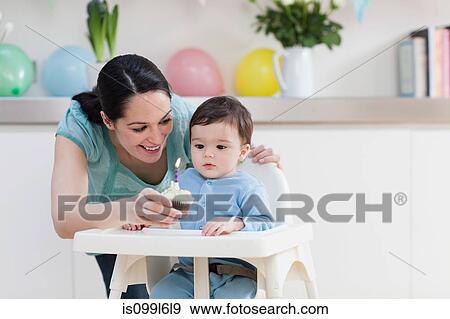 Mother giving birthday cupcake to baby son in high chair View Large Photo Image Stock Photo - Mother giving birthday cupcake to baby son in high chair. Fotosearch