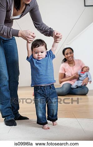 Stock Image - Mother helping baby son to walk. Fotosearch