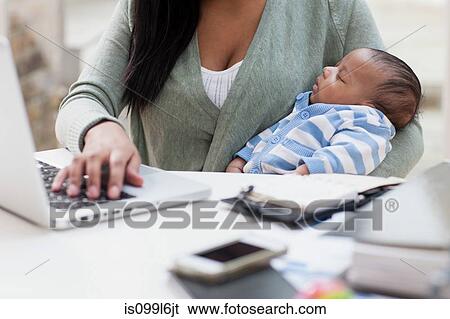 Stock Photograph - Mother holding baby and using laptop. Fotosearch