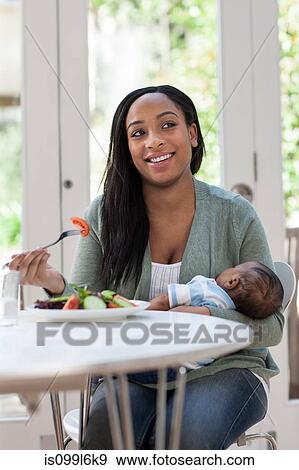 Stock Photo - Mother holding baby son and having lunch. Fotosearch