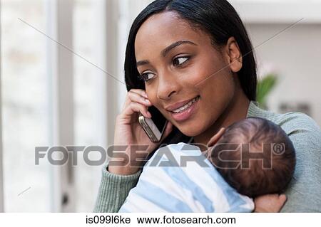 Stock Image - Mother on cellphone, holding baby son. Fotosearch