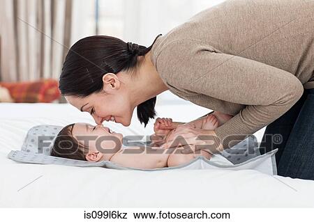 Stock Photo - Mother rubbing noses with baby boy on changing mat. Fotosearch