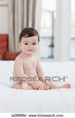 Stock Photograph - Portrait of a baby boy sitting on bed. Fotosearch