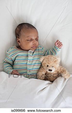 Stock Photograph - Sleeping baby in bed with teddy bear. Fotosearch