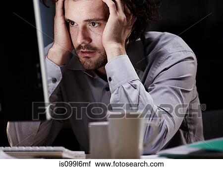 Stock Image - Stressed young man, working late. Fotosearch