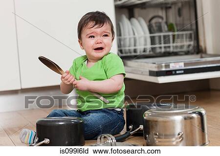 Stock Image - Upset baby on floor with saucepans and wooden spoon. Fotosearch