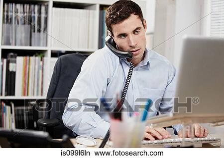Young man on telephone and working on laptop View Large Photo Image Picture - Young man on telephone and working on laptop. Fotosearch