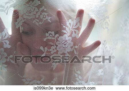 Stock Image - Young woman behind lace curtain. Fotosearch