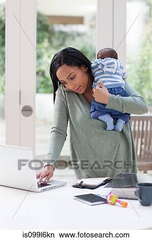 Picture - Young woman holding baby and using laptop. Fotosearch