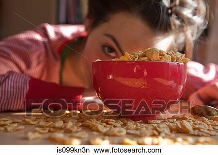 Picture - Young woman looking out from behind bowl and spilt breakfast cereal. Fotosearch