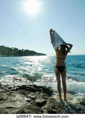 Stock Image - Young woman taking off t-shirt by the sea. Fotosearch