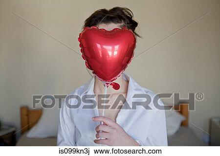Young woman with heart shaped balloon in front of her face View Large Photo Image Stock Image - Young woman with heart shaped balloon in front of her face. Fotosearch