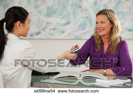 Art dealer taking credit card from young woman at desk in gallery View Large Photo Image Picture - Art dealer taking credit card from young woman at desk in gallery. Fotosearch