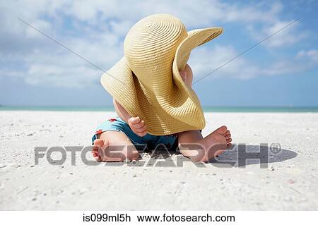 Stock Image - Baby boy playing with mother's sun hat on the beach. Fotosearch