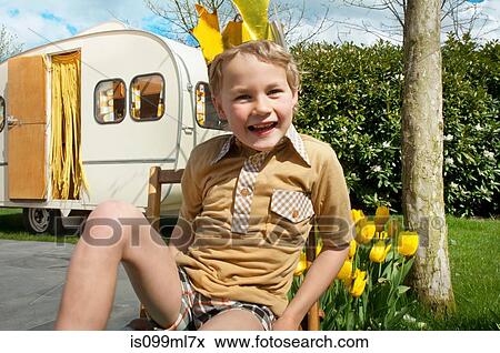 Stock Photo - Boy sitting outside caravan wearing party hat. Fotosearch