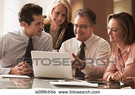 Stock Image - Business colleagues working on laptop on desk, smiling. Fotosearch