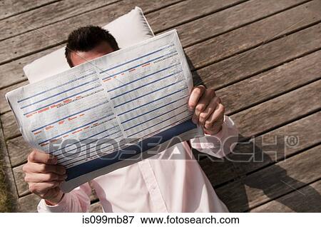 Stock Photo - Businessman lying on decking reading newspaper. Fotosearch