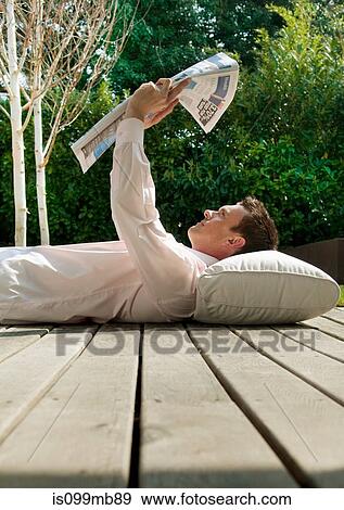 Stock Photo - Businessman lying on decking reading newspaper. Fotosearch