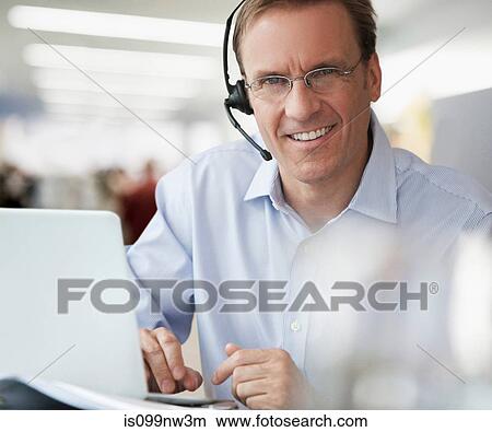 Businessman using laptop and wearing headset, portrait View Large Photo Image Picture - Businessman using laptop and wearing headset, portrait. Fotosearch