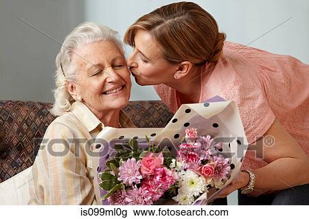 Stock Image - Daughter giving senior mother bouquet of flowers. Fotosearch
