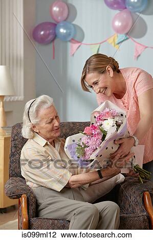 Stock Image - Daughter giving senior mother bouquet of flowers. Fotosearch