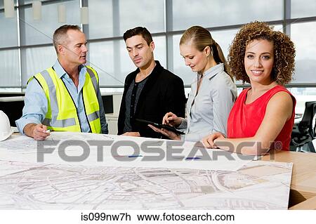 Stock Image - Engineer with architects looking at blueprints and digital tablet in office. Fotosearch