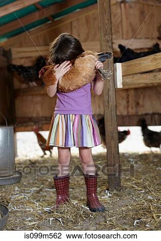 Stock Image - Girl holding hen in hen house. Fotosearch