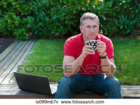 Man with laptop holding mug, portrait View Large Photo Image Stock Photo - Man with laptop holding mug, portrait. Fotosearch